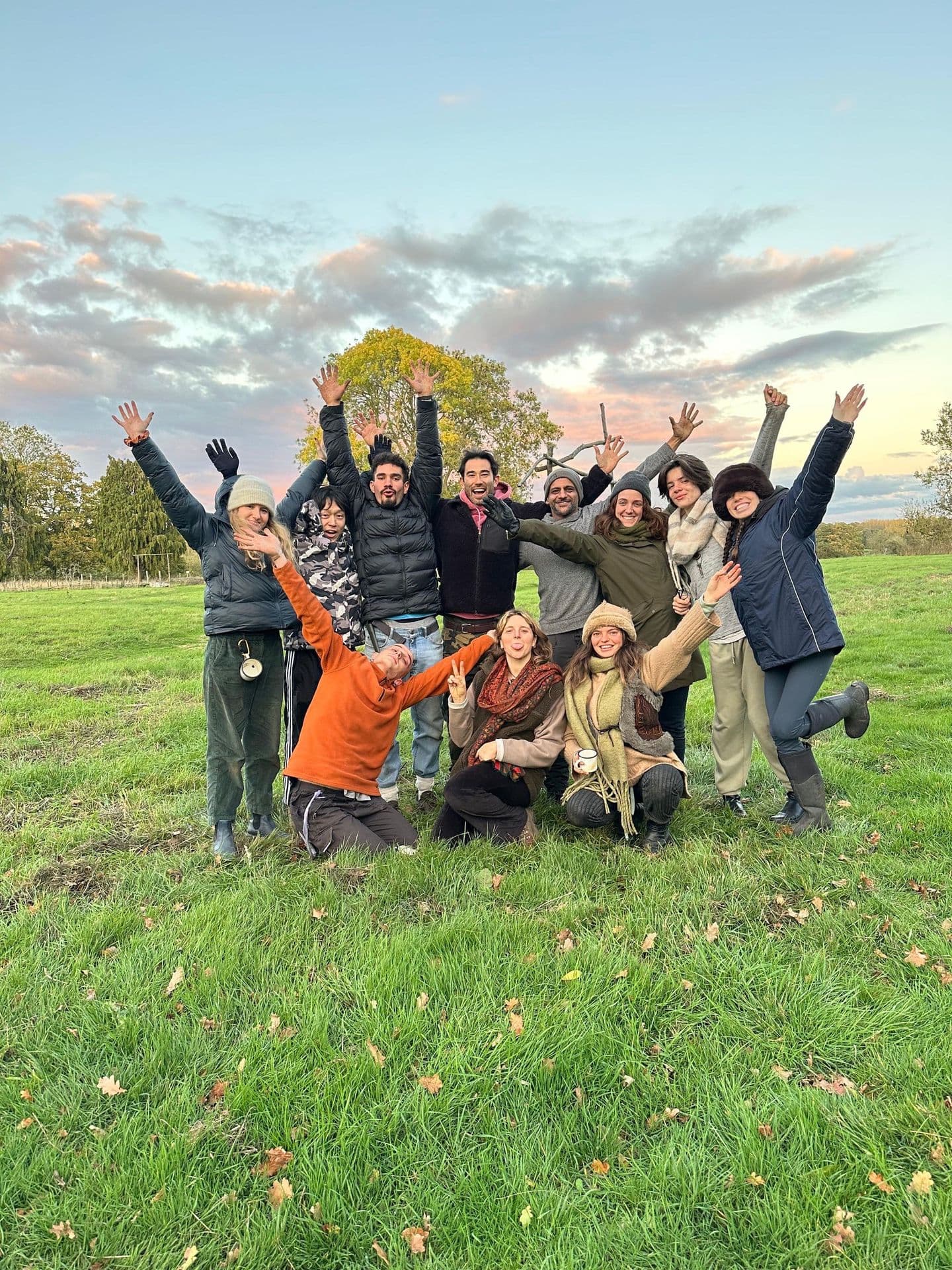 A group with arms raised joyfully at sunset — the Wilding community