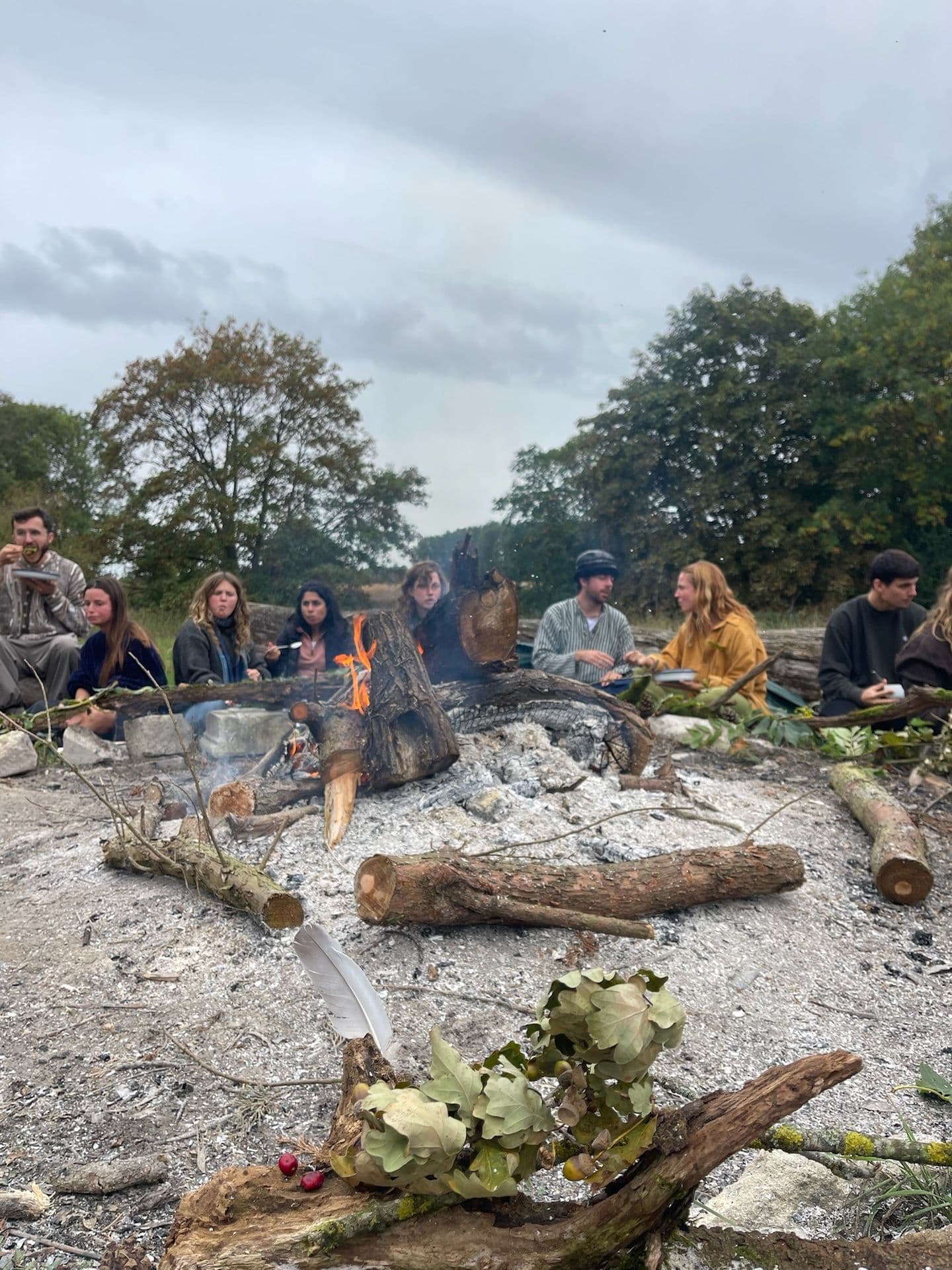 Daytime fireside gathering — embers glowing, people relaxed