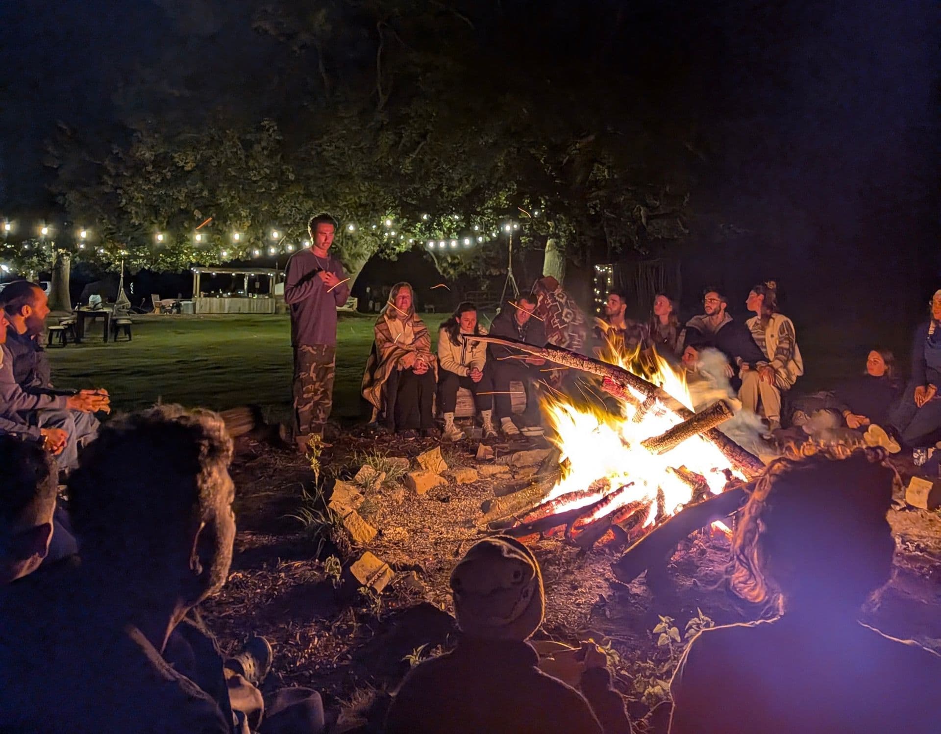 Harry speaking to a group around a roaring campfire at night